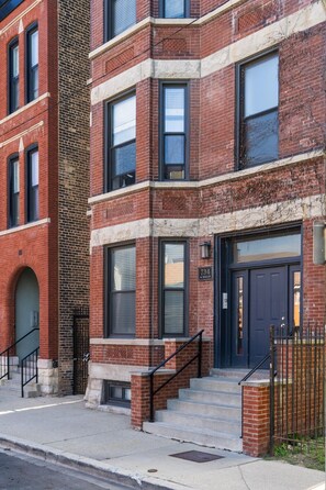 A multi-story brick building with a black front door, a visible address sign, and a small set of stairs leading to the entrance. - Flexhome West Town Spacious 2BR Duplex · Sleeps 8 (Chicago)
