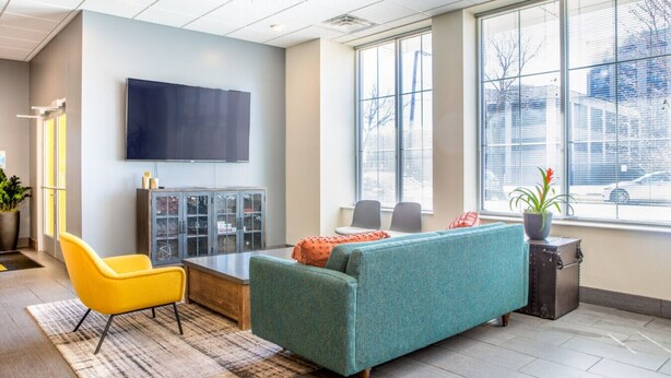 A modern office space with a teal sofa, yellow chair, and a flat-screen TV on the wall. - Modern Walker`s Point Studio with Gym and Balcony (Milwaukee)