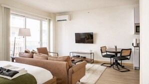 A hotel room with a bed, a sofa, a desk, a chair, a TV, and an air conditioning unit. - Modern Walker`s Point Studio with Gym and Balcony (Milwaukee)