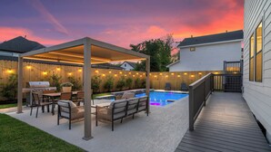 En have med pool, overdækket terrasse, grillområde og udendørs siddepladser.