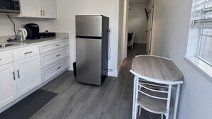 Eine kleine Küche mit weißen Schränken, einem Edelstahlkühlschrank, einer eingebauten Mikrowelle und einem Deckenventilator.