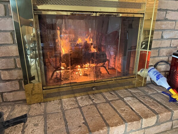 En öppen spis med ett glasskydd, en tegelvägg och en flaska rengöringsmedel på golvet.