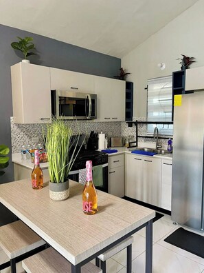 A modern kitchen with white cabinets, a stainless steel refrigerator, a microwave, and a sink. There are two bottles of orange juice and a potted plant on the counter. - Soothing 2-bedroom house with AC in charming Portmore (Portmore)