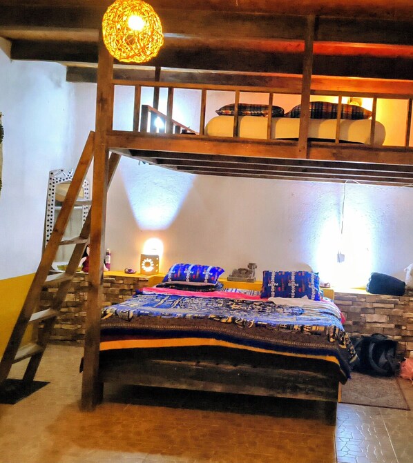 Un lit superposé avec une échelle en bois, une couvre-lit à motifs et un luminaire fixé au mur.