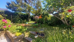 A garden with various plants, a wooden deck, and a bird feeder. - Dependent room at the bottom of the garden (Perros-Guirec)