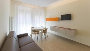 A modern living room with a sofa, a dining table with chairs, a TV mounted on the wall, and a cabinet with a decorative top. - San Felice 135 - 4 (Bologna)