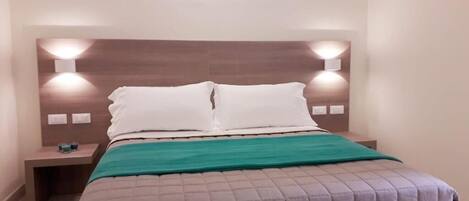 A neatly made bed with a headboard, two bedside tables, and a green throw blanket.