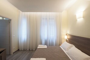 A hotel room with a bed, curtains, a wall-mounted lamp, and a door. - San Felice 135 - 4 (Bologna)