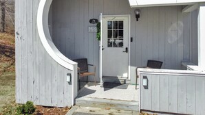 Un bâtiment en bois peint en blanc, doté d’une grande entrée en arc de cercle, d’une porte avec une fenêtre et d’un petit porche abritant une chaise.