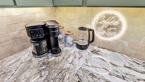 Une cuisine équipée d’une machine à café, d’une bouilloire et d’un néon décoratif sur le thème du café.