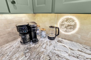 A kitchen with a coffee maker, a kettle, and a coffee-themed neon sign.