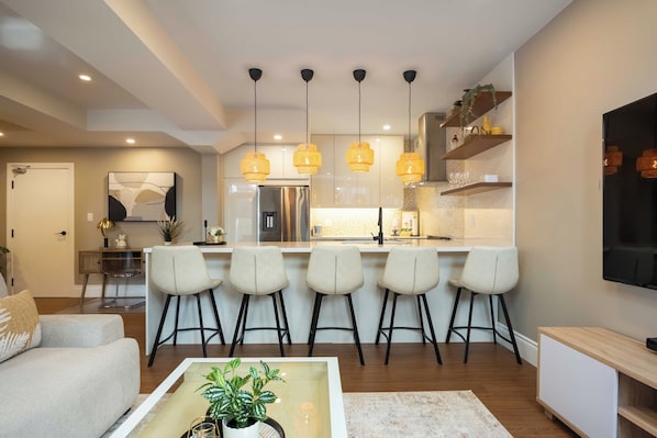 A modern kitchen with a central island, pendant lights, and bar stools.