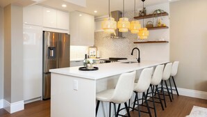 Een moderne keuken met een centraal eiland, roestvrijstalen apparatuur, hanglampen en barkrukken.