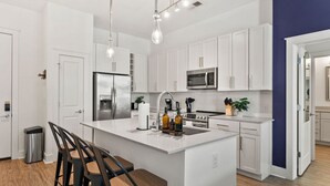 A modern kitchen with white cabinets, stainless steel appliances, a central island with bar stools, and pendant lighting. - Carolina Charm - Free Parking, Pool, Gym (Charlotte)