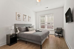 Un dormitorio moderno con cama, mesita de noche, lámpara y un escritorio con silla.