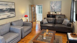 Un salon avec deux canapés gris, une table basse en verre ornée de bougies, une table d’appoint en bois avec une lampe rouge et un tableau accroché au mur.