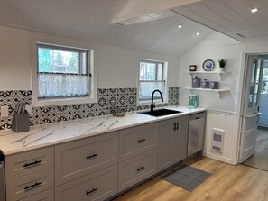 A kitchen with two windows, a sink, and a coffee maker.