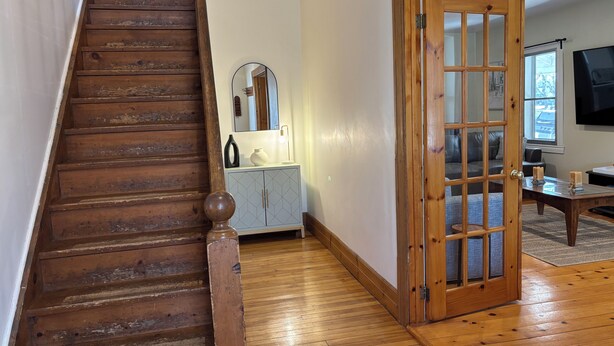 Un escalier en bois mène à une pièce où se trouvent un meuble gris, un miroir et une porte en bois.