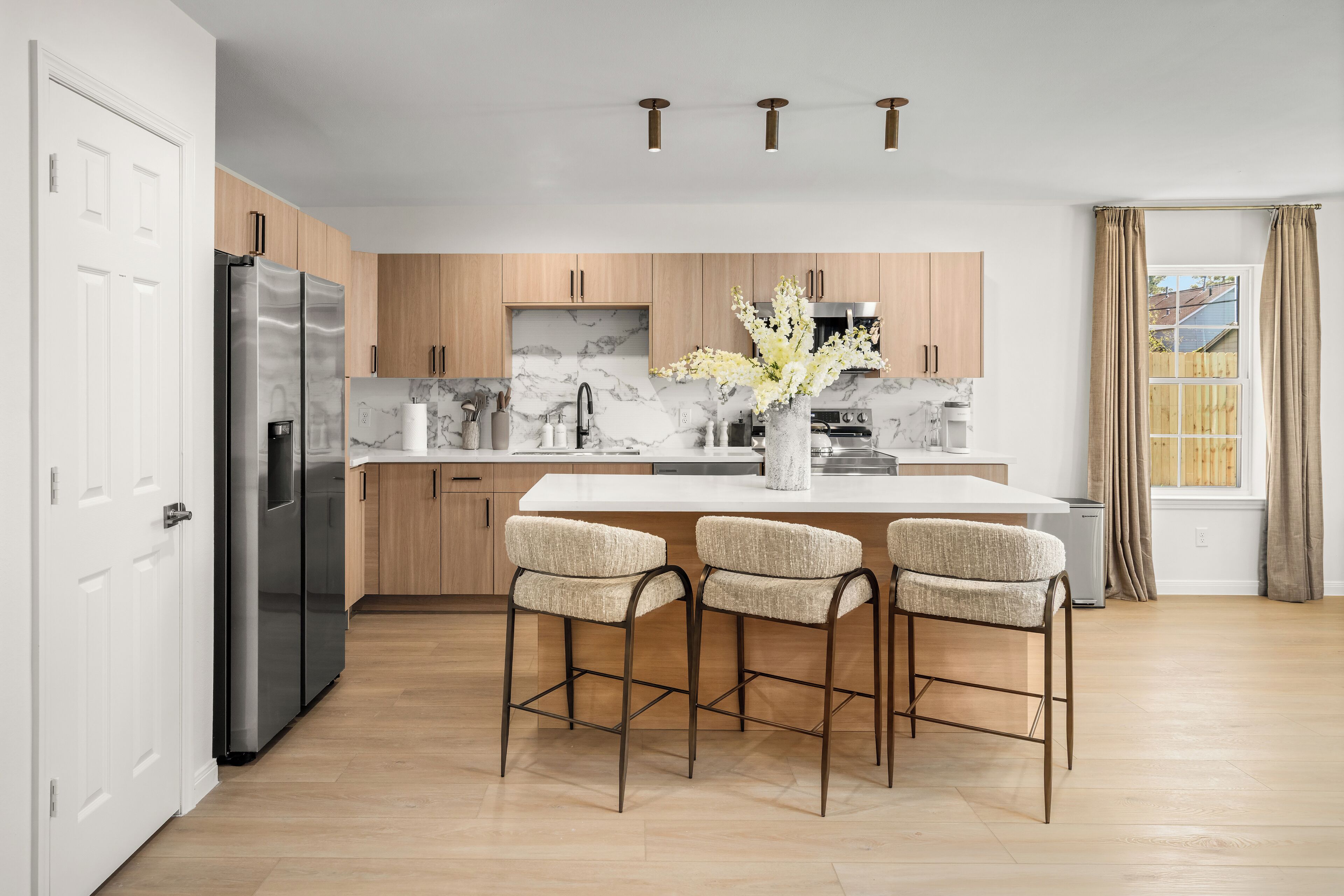 A modern kitchen with a marble backsplash, stainless steel appliances, wooden cabinets, and a central island with bar stools.