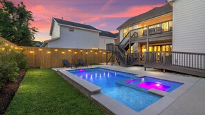 A backyard with a swimming pool, wooden deck, and a two-story house with a balcony.