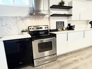A modern kitchen with a stainless steel stove, a dishwasher, and a sign that reads 'THIS HOME RUNS ON LOVE LAUGHTER AND LOTS OF STRONG COFFEE.' - Iron & Oak Suite Minutes from Silverstar Skii Resort  Lakes, Hiking &Restaurant (Vernon)