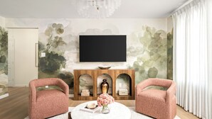A living room with a TV, two armchairs, a coffee table, and a fireplace with decorative items. - Resort-Style • 4BR • Heated Pool/Spa • Makeup Room (Houston)