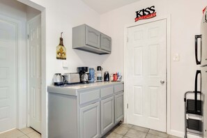 A kitchen with grey cabinets, a coffee maker, a kettle, and a toaster. There is a door with a sign above it. - Modern NOLA House with Yard, Your Mardi Gras Base (New Orleans)