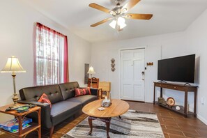 A living room with a sofa, coffee table, TV, and ceiling fan. - Modern NOLA House with Yard, Your Mardi Gras Base (New Orleans)