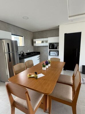 A modern kitchen with a dining table, chairs, and a refrigerator. - Apartment for seasonal rental in Porto Seguro, Taperapuan Beach. 800 meters from the sea. (Porto Seguro)