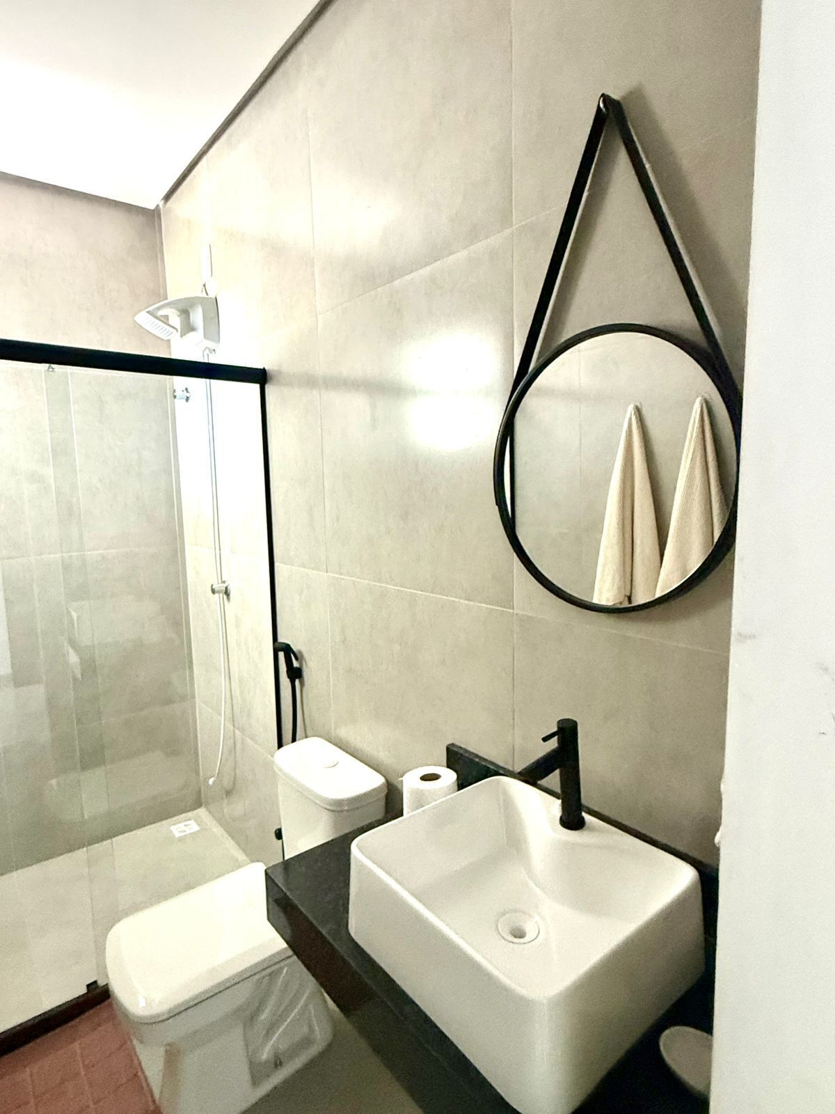 Ein modernes Badezimmer mit Duschkabine aus Glas, Toilette in Weiß, Waschbecken in Weiß und einem runden Spiegel.