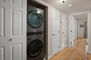 Une buanderie avec des machines à laver et des sèche-linge superposés, des portes blanches et un plancher en bois.