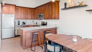 A modern kitchen with wooden cabinets, a stainless steel refrigerator, a microwave, and a bar area with stools. - Lake View 3BR/2BA in Incline Village, Fireplace (Incline Village)