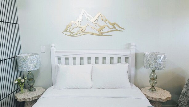 A bed with white bedding, two bedside tables with lamps, and a wall decoration of mountains. - Perfect 1-bedroom basement with AC in pleasant Burnaby (Burnaby)
