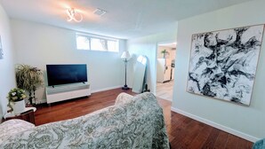 A living room with a flat-screen TV, a patterned sofa, a large abstract painting, and a potted plant. - Perfect 1-bedroom basement with AC in pleasant Burnaby (Burnaby)