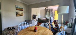 Un salon comprenant un canapé, des fauteuils, une table à manger avec un objet rouge, un téléviseur et un ventilateur de plafond.