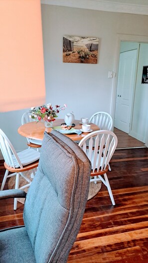 Un coin repas avec une table ronde, des chaises blanches, un vase de fleurs, une théière et une tasse.