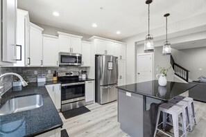 A modern kitchen with white cabinets, stainless steel appliances, a granite countertop, and a black island. - Jubilee Retreat+7 King Suites+Sleeps 24+Hot Tub+Table Rock Lake+Game Room (Branson)