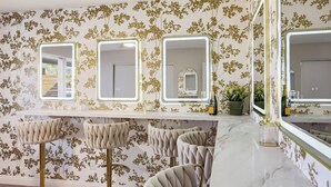 Un bagno con tre specchi, un mobile lavabo con specchio e un'area salotto con sgabelli da bar.