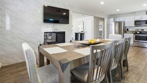 Una cucina moderna con TV a schermo piatto, elettrodomestici in acciaio inossidabile e zona pranzo con schienale in marmo e tavolo in legno.