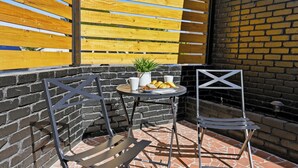 Un patio con due sedie in metallo, un piccolo tavolino rotondo con una pianta e un piatto di cibo, e un muro in mattoni.
