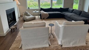 Een woonkamer met een open haard, een hoekbank, een salontafel en uitzicht op een groen landschap.