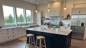 Een moderne keuken met een groot eiland, houten krukken en een roestvrijstalen koelkast.