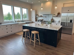 Una cucina moderna con un'isola grande, sgabelli di legno e un frigorifero in acciaio inossidabile.