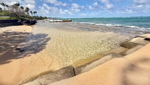 A beach with clear water, a rocky outcrop, and palm trees. - Oceanfront Two-Bedroom Condo, Steps from the Sand and Pool (Kapaʻa)