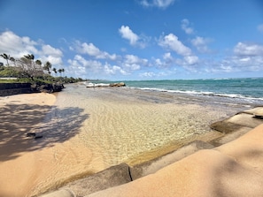A beach with clear water, a rocky outcrop, and palm trees. - Oceanfront Two-Bedroom Condo, Steps from the Sand and Pool (Kapaʻa)