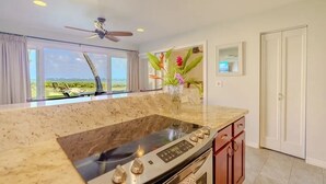 A modern kitchen with a large island, a ceiling fan, and a view of the ocean. - Oceanfront Two-Bedroom Condo, Steps from the Sand and Pool (Kapaʻa)