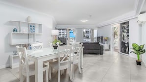 A spacious living area with a dining table, chairs, a sofa, and a balcony with a view. - Moroccan Surfers - 3BR Apartment (Surfers Paradise)