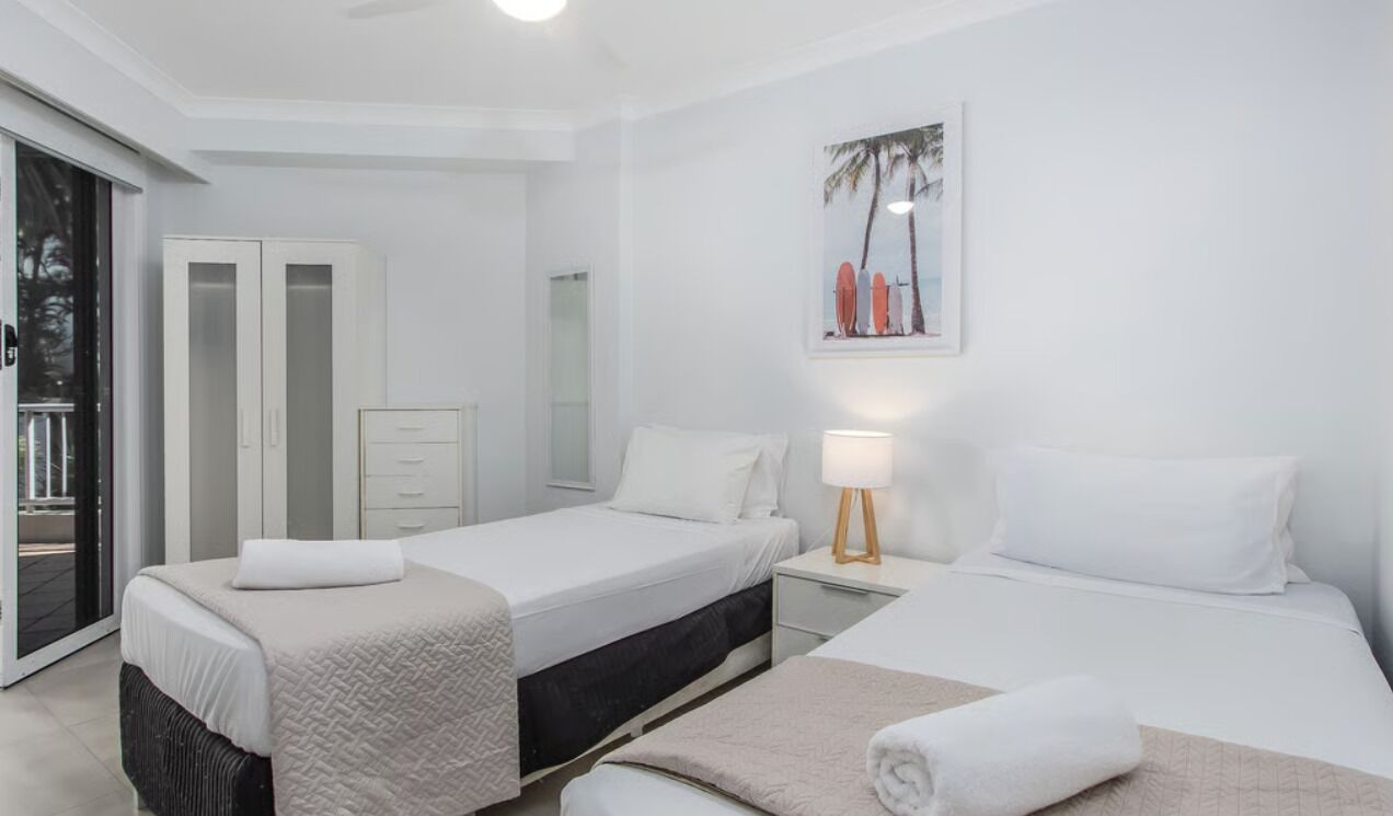 Ein Hotelzimmer mit zwei Betten, einem Nachttisch, einer Lampe, einem Kleiderschrank und einer Glasschiebetür, die zu einem Außenbereich führt.