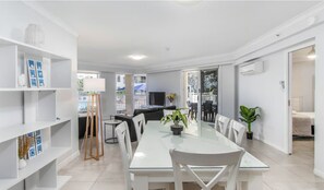 Uma sala de jantar moderna com mesa de vidro, cadeiras brancas e um aparador branco.