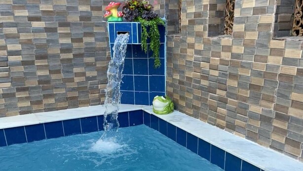 Een zwembad met een waterval, omringd door een betegelde muur met een geometrisch patroon.